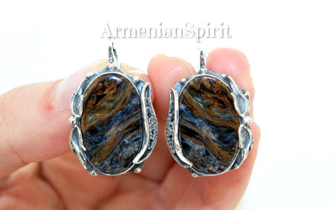 Pietersite is a rare gemstone with waves blue and brown slighly shiny and sparkling. These earring are handcrafted and has unique design. There is a flower design around the oval pietersite gemstone. The lock of these blue pietersite earrings is English lock, also called leverback.