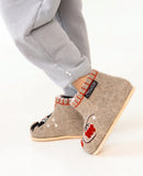 Beige woolen bootie indoor slippers with floral design worn by a person in gray pants on a white background