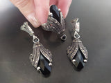 A pair of silver earrings  and ring featuring black onyx and marcasite details, displayed against a dark background.