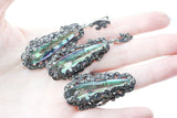 A set of long silver earrings with marcasite accents and a nacreous green topaz, alongside a matching ring, displayed on a person's hand.