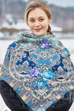 A woman wearing a navy and light blue floral merino wool scarf around her neck with a geometric patterned design with large peony flowers.