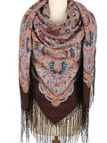 Paisley patterned shawl with fringe on a mannequin against a white. background. A woman wearing this large brown shawl feels warm and elegant. The light blue and red traditional Slavic pattern stands out beautifully, and the silky fringe adds gentle movement.