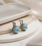Pair of silver earrings with larimar blue stones and gold plated details made by Armenian artisans on a white surface.