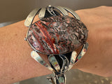 Silver bracelet with a large, textured terracotta red stone on a wrist against a neutral background