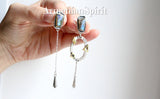 A pair of silver earrings featuring labradorite gemstones with gold-plated accents and a ring attached to the top. The earrings have a loop closure and are placed against a dark background with the text 'ArmenianSpirit' visible.