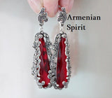 A close-up of a silver earrings displaying exceptional filigree craftsmanship around long, transparent red gemstones. The combination of oxidized silver textures and glittering marcasite borders gives the ring and earrings an authentic antique look. Ideal for collectors of unique ethnic and vintage jewelry.