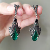 A pair of silver earrings featuring black onyx and marcasite, held in a person's hand.