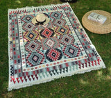 Patterned Armenian woven rug on grass with a hat and bag nearby.. The pattern is traditional daraz ornament in white, red and blue which are usual pattern colors in Armenian heritage.