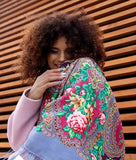 A woman wearing a beautiful Slavic ethnic shawl woven from 100% merino wool. The natural sheep wool displays delicate pink peony flowers in vintage style against blue-gray shades.