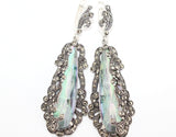 A set of long silver earrings with marcasite accents and a nacreous green topaz, alongside a matching ring, displayed on a person's hand.