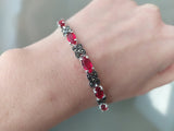 A sterling silver 925 bracelet featuring red lab topaz stones and Marcasite details, worn on a person's wrist.