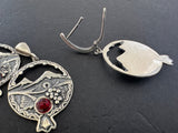 Silver earrings with Masis mountain designs on a dark surface