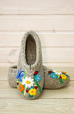 Pair of felted slippers with floral embroidery on a wooden surface