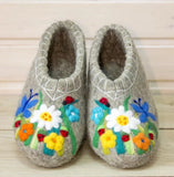 Pair of gray felted slippers with floral and butterfly designs on a wooden surface