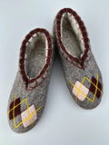 Men large woolen slippers slip on made from merino wool felt in gray color with brown and beige rhombus design embroidery on a white surface.