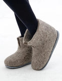 Gray felted very large size slippers for men worn with black tights on a white background. The slippers look like house boots.
