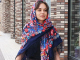 A woman wrapped in oversized merino wool shawl, adorned with deep blue and red vintage floral patterns inspired by Slavic traditional art. Soft, warm, and generously sized, the head and shoulders shawl drapes beautifully over the shoulders, creating a striking silhouette for the modern woman who loves heritage style.
