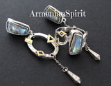 A pair of silver earrings featuring labradorite gemstones with gold-plated accents and a ring attached to the top. The earrings have a loop closure and are placed against a dark background with the text 'ArmenianSpirit' visible.