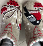 Pair of natural wool slippers with embroidered designs of a bird and flowers on a neutral background