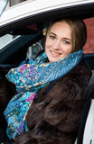 Woman wearing a decorative blue scarf and fur coat sitting in a car.