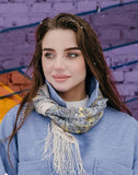 Woman wearing a blue coat and patterned pale yellow and gray neck  scarf with a snowy background.