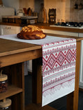 A white table runner with a red and green geometric Nordic pattern draped over a wooden kitchen island, with a loaf of bread placed on top.