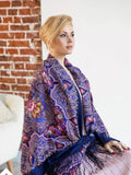 Woman wearing a colorful patterned shawl in a room with a brick wall. Traditional Slavic purple shawl in merino wool. Light blue and pink ornament, large size, soft, warm, with silky fringe for wrapping.