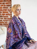 Woman wearing a colorful patterned shawl in a room with a brick wall. Traditional Slavic purple shawl in merino wool. Light blue and pink ornament, large size, soft, warm, with silky fringe for wrapping.