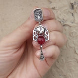 A pendant Armenian featuring garnet stones and pomegranate-shaped designs, held in a person's hand.