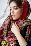 Close-up portrait of a woman wearing a cozy, thick woolen shawl adorned with large pink, green, and orange vintage Slavic roses over a black background.