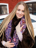 A Slavic blond woman wearing a patterned scarf and fur coat with a blurred background. Purple shawl for women, natural merino wool, Slavic traditional pattern in light blue and red. Large and comfortable with silky fringe.