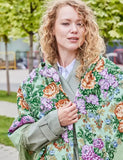 Portrait of a woman wrapped in a warm, square merino wool scarf with a green and purple rose flower pattern and beige fringes.