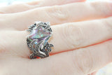 A silver ring with a pale green nacreous Marcasite centerpiece, displayed on a person's hand.