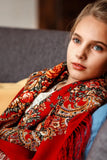 Young girl wearing a red floral embroidered shawl sitting on a couch.