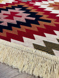 Close-up of a colorful patterned rug with cotton fringes on a wooden floor.