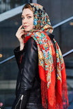 Woman wearing a colorful headscarf and black leather jacket against a blurred background. The scarf depict the vintage flowers in yellow and blue.