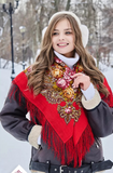 Woman wearing a red scarf and winter clothing in a snowy park. A woman wearing a beautiful ethnic Slavic shawl made of 100% merino wool. The natural sheep wool shines in rich red tones with delicate floral patterns.