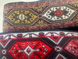 Close-up of two woven textile bands with geometric Armenian carpet patterns. The top band features beige, black, and red motifs, while the bottom band is primarily red, black, and white.