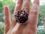 A set of sterling silver jewelry including oxidized black net design earrings and a matching ring, each adorned with a red garnet stone.