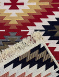 Close-up of a patterned  rug with geometric design featuring red, beige, black, and white colors.