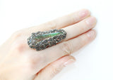 Long luxury silver ring with marcasite accents and a nacreous green topaz displayed on a person's hand.