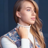 A photo showing a woman with long light brown hair wearing a white ribbed turtleneck and a blue patterned sleeveless woolen vest.