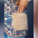 A close-up of a person wearing a blue and white floral patterned garment with a beige sherpa fleece pocket.