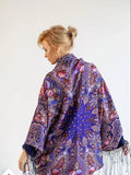 Woman wearing a floral patterned shawl on a white background. Purple merino wool shawl with light blue and red Slavic pattern. Large, warm, wrapping shawl with silky fringe. Traditional folk style.