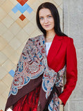 Extra large wrapping shawl made of merino wool and silky fringe with brown and turquoise herbal pattern. This brown shawl in natural merino wool features light blue and red Slavic patterns. A woman wearing it enjoys its warmth, soft feel, and flowing silky fringe. Large and easy to wrap.