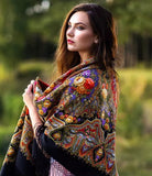 Woman wearing a colorful woolen shawl in an outdoor setting. A woman wearing a black merino shawl with large peony flowers in red and yellow with green leaves looks elegant and classy. The black fringe and large size make it perfect for wrapping.