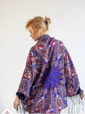 Woman wearing a floral patterned shawl on a white background. Purple merino wool shawl with light blue and red Slavic pattern. Large, warm, wrapping shawl with silky fringe. Traditional folk style.
