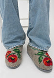 Gray authentic sheep wool slippers with poppy flower floral design worn with blue jeans on a white background