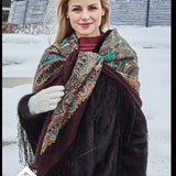 Woman wearing a patterned scarf and fur coat in a snowy setting. Warm, soft, and full of character, this brown shawl with turquoise ethnic patterns is perfect for a boho wardrobe. A woman wearing it gets a relaxed, traditional folk look with a modern bohemian touch.