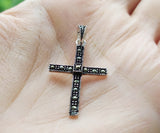 A sterling silver cross pendant with Marcasite stones, held in a person's hand.